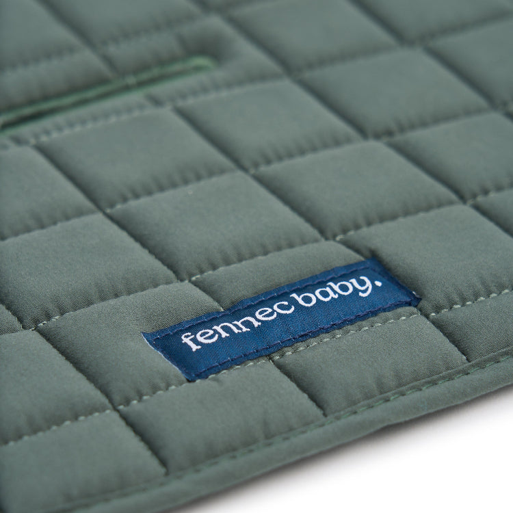A close-up of a sage green quilted baby pram liner with a blue fabric brand label reading 'fennec baby.' on a white background.
